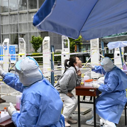 Health workers take swab samples from people to be tested for Covid-19 coronavirus at a makeshift testing site along a street in Beijing on May 11, 2022. (Photo by Jade GAO / AFP)