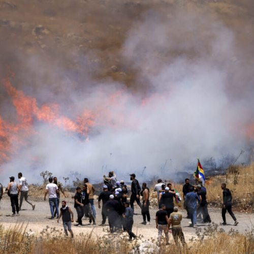 Members of Syria's Druze community walk through tear gas fumes released by Israeli forces to disperse them, as they gather along the dividing line to attempt to cross the barbed-wire fence with the Israeli-annexed Golan Heights near Majdal Shams on July 16, 2025. Israeli troops on July 16 sought to control crowds and prevent Druze from crossing the border with Syria, after deadly violence in the country's south that prompted Damascus to send in government forces. (Photo by Jalaa MAREY / AFP)