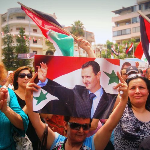 A handout picture released by the official Syrian Arab News Agency (SANA) on May 29,2014 shows citizens, one holding a poster bearing the portrait of Syrian President Bashar al-Assad, during a rally to support his re-election on May 29, 2014 outside the city hall of Syria's Mediterranean port city of Latakia.  Assad faces two little known challengers in next month's vote and is widely expected to clinch a third seven-year term in office despite the raging civil war.  AFP PHOTO/HO/SANA == RESTRICTED TO EDITORIAL USE - MANDATORY CREDIT "AFP PHOTO / HO / SANA" - NO MARKETING NO ADVERTISING CAMPAIGNS - DISTRIBUTED AS A SERVICE TO CLIENTS ===