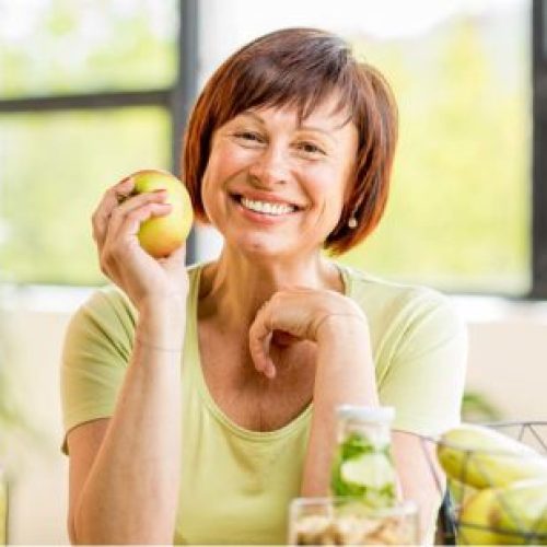 Portrait of a beautiful older woman with green healthy food on the table indoors on the window background