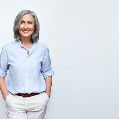 Smiling beautiful mature business woman standing isolated on white background. Older senior businesswoman, 60s grey haired lady professional female ceo, coach looking at camera, banner, copy space.