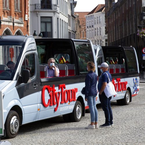 A tour operator in a protective face mask sits in an empty tour bus as he speaks with a couple on the market square of Bruges, Belgium, Monday, Aug. 24, 2020. Europe’s leanest summer tourist season in history is starting to draw to a close, six months after the coronavirus hit the continent. COVID-19 might tighten its grip over the coming months, with losses piling up in the tens of billions of euros across the 27-nation European Union. In the Belgian city of Bruges, white swans instead of tourist boats rule the canals, hotels stand empty and museums count their losses. (AP Photo/Virginia Mayo)