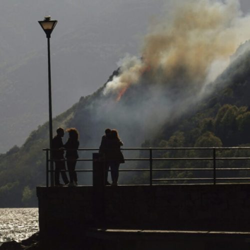 People watch from the Piona shore as a wind powered fire burns on the Olgiasca hill, near Colico, northern Italy, Italy, Monday, April 18, 2022. (AP Photo/Luca Bruno)