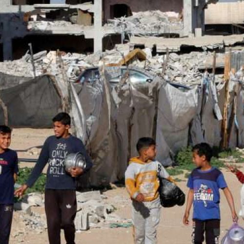Palestinian children walk with containers to receive food cooked by a charity kitchen, during the Muslim holy month of Ramadan, in Rafah, in the southern Gaza Strip, March 13, 2025. REUTERS/Hatem Khaled