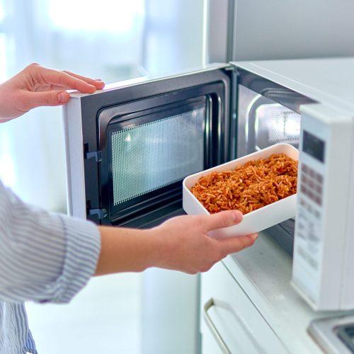 Warming up a container of food in the modern microwave oven for snack lunch at home