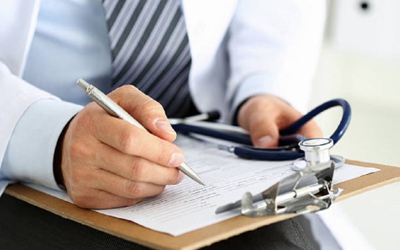 Male medicine doctor hand holding silver pen writing something on clipboard closeup. Ward round, patient visit check, medical calculation and statistics concept. Physician ready to examine patient