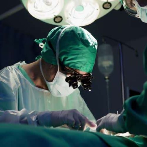 attending Doctors surgeons team are performing surgical operation in hospital operating room - senior male physician wearing magnifier is concentrating on work