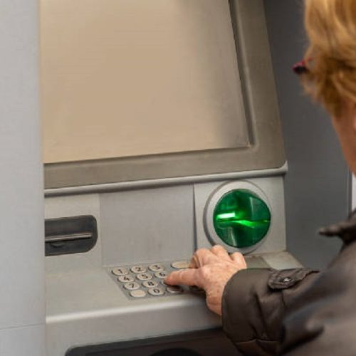 Close up, an elderly woman uses an ATM