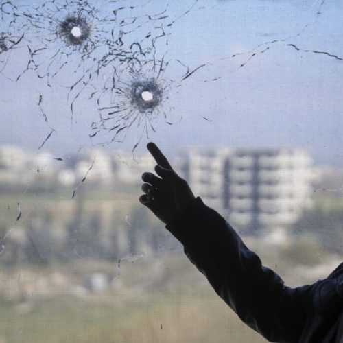 A nurse points to bullet holes in a window following the recent wave of violence between Syrian security forces and gunmen loyal to former President Bashar Assad, as well as subsequent sectarian attacks, at a hospital in the town of Jableh, in Syria's coastal region, on Monday, March 10, 2025. (AP Photo/Omar Albam)