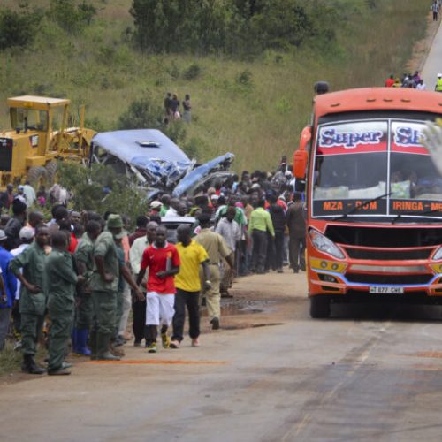 A police officer keeps traffic and people away from the scene of a bus crash, center-left, near Changarawe village in the Mafinga District of the Iringa region of Tanzania, Wednesday, March 11, 2015. A Tanzanian police official says dozens of people were killed when a truck carrying a shipping container rammed into the bus. (AP Photo)